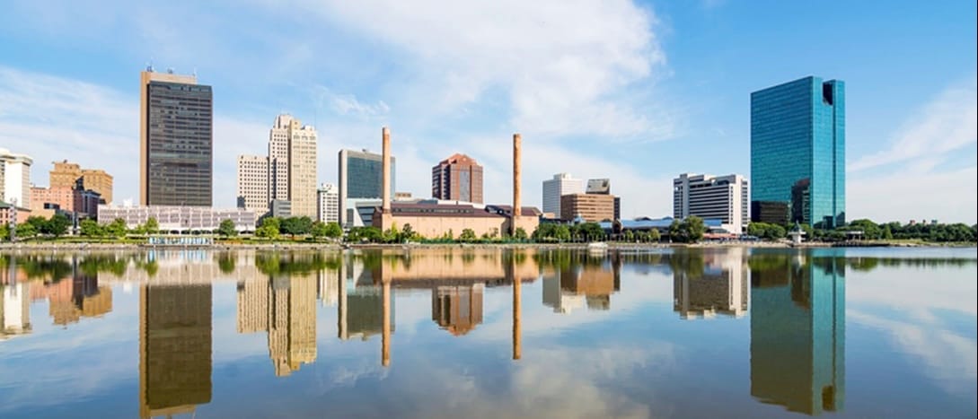 A panoramic view of downtown Toledo Ohio's skyline reflecting into the Maumee river. A beautiful blue sky with white clouds for a backdrop.