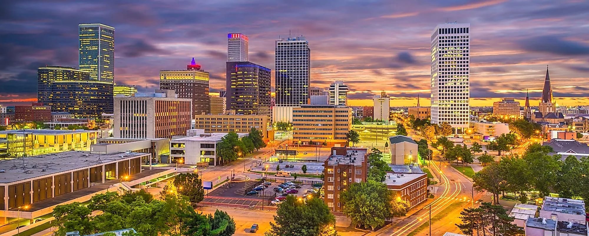 Beautiful Skyline of Tulsa, Oklahoma at Sundown. The streets appear gold from the lights and final flashes of light from the setting sun. Lights from the building are still on from the day. 