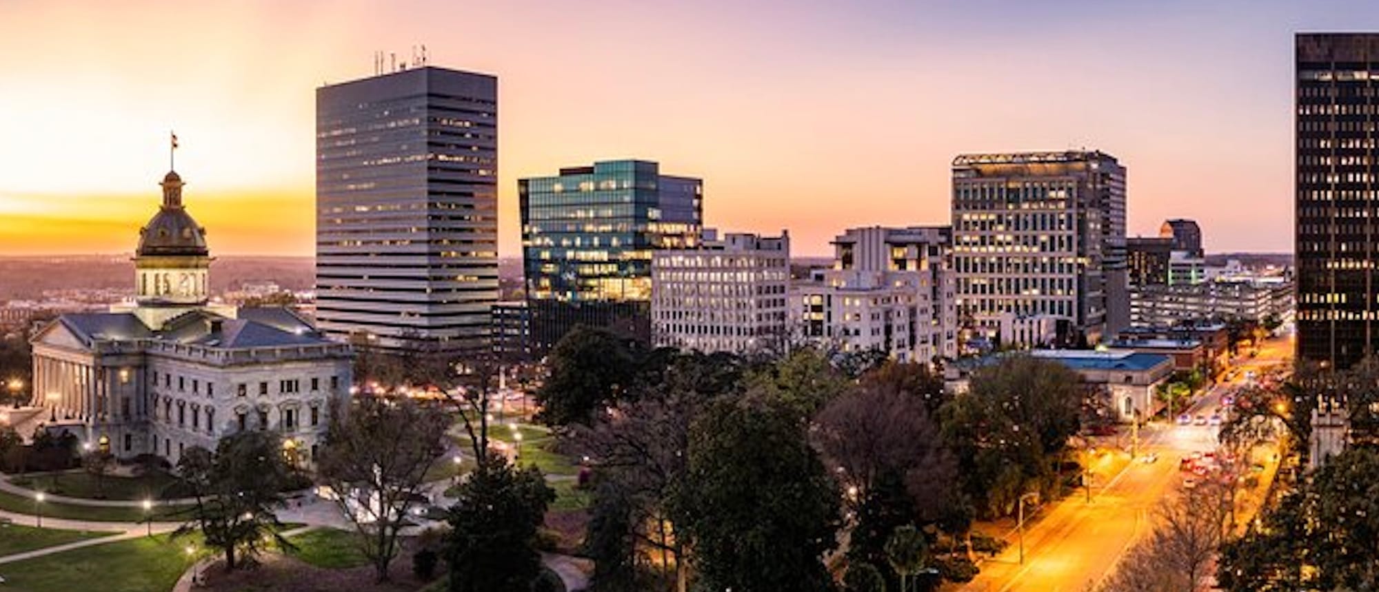 Downtown Columbia, South Carolina at Dusk. Capitol Building is on the left and downtown buildings are in the center. Main downtown street appears gold as the street lights illuminate the street. 