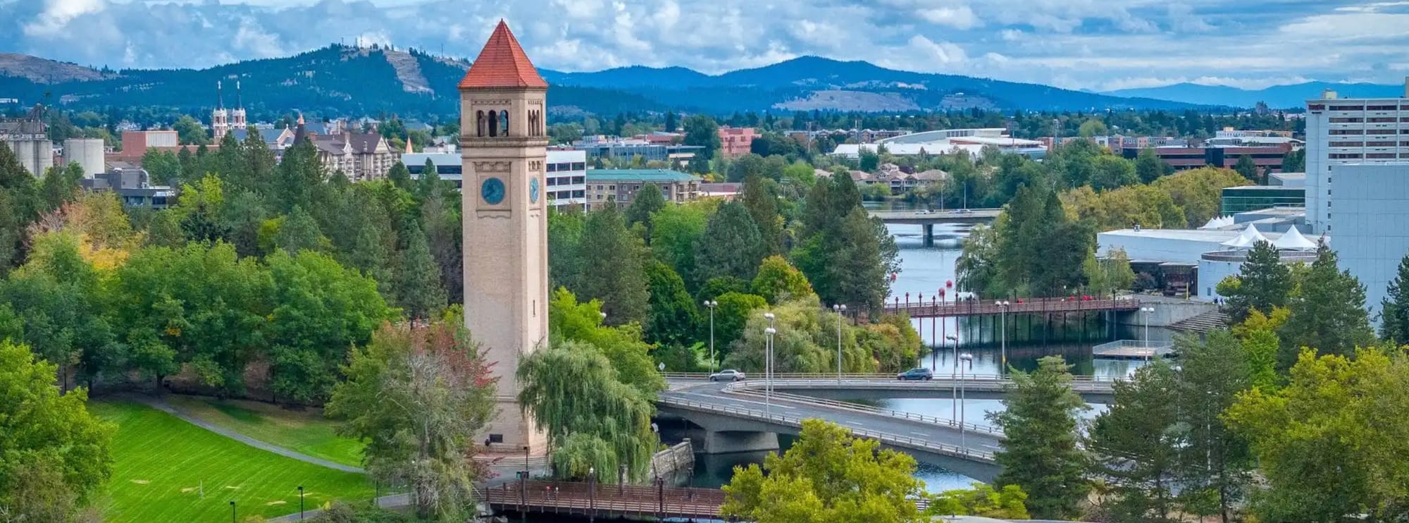 Aerial View of Spokane Washington. Great Northern clock tower in Riverfront Park dominates the image. The Spokane River runs along the right side of the image and the mountains are in the background.  