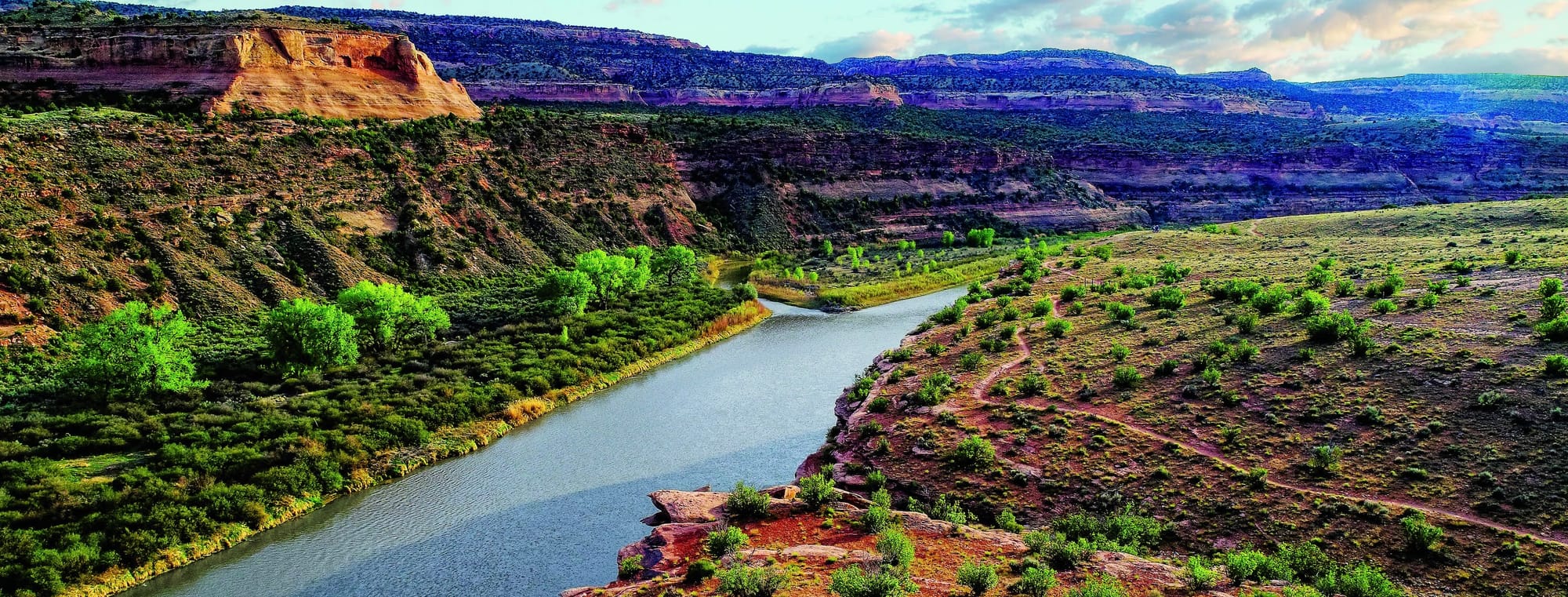 Image of Sunrise on the Gunnison River in Grand Junction, Colorado. Mountain plateaus run along and behind the left side of the river bank. 
