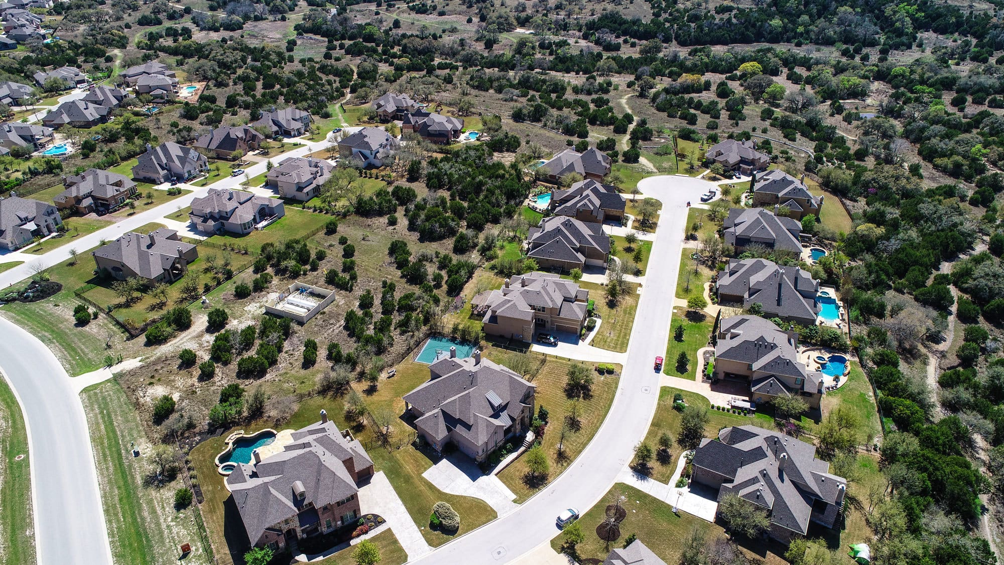Circle C Ranch Aerial with Suburban Homes with Pools in the Foreground and Trails and Trees in the Background. 