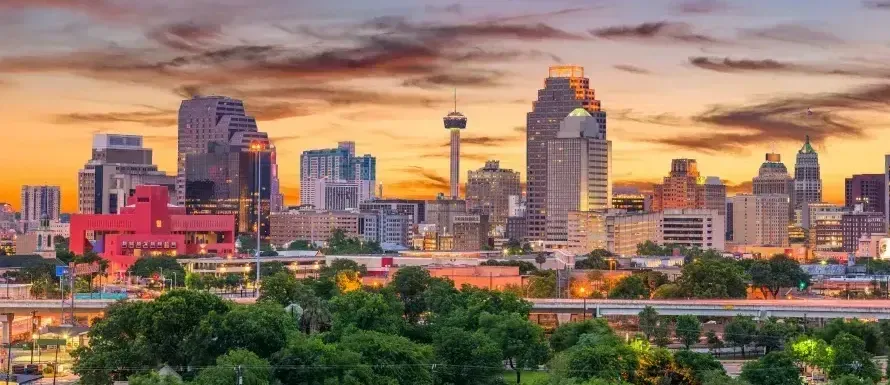 Beautiful image of the Skyline of San Antonio at Sundown. Greenery in the foreground and tall buildings of the city in the background. 