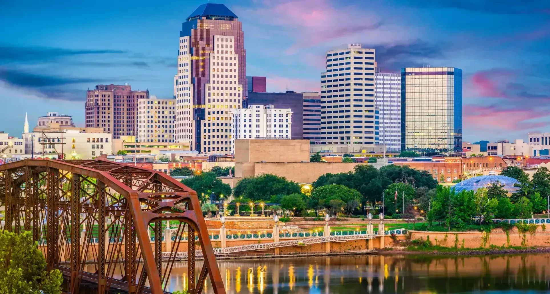 Beautiful Image of the Skyline of Shreveport, Louisiana. The Red River is in the foreground and shows the reflection of the city as the sun settles. The city buildings are in the background across the river. 
