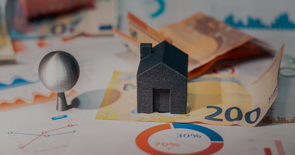Una casa en miniatura sobre billetes, junto a un gráfico de torta repartido