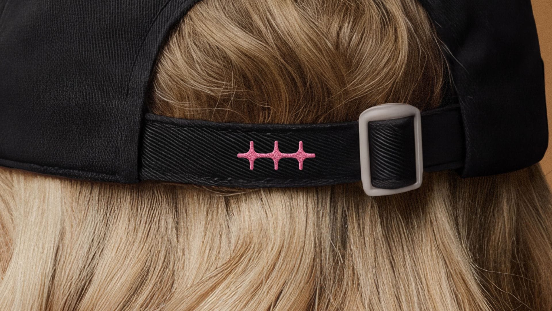 The new n8n logo mark embroidered in pink on the strap of a black cap