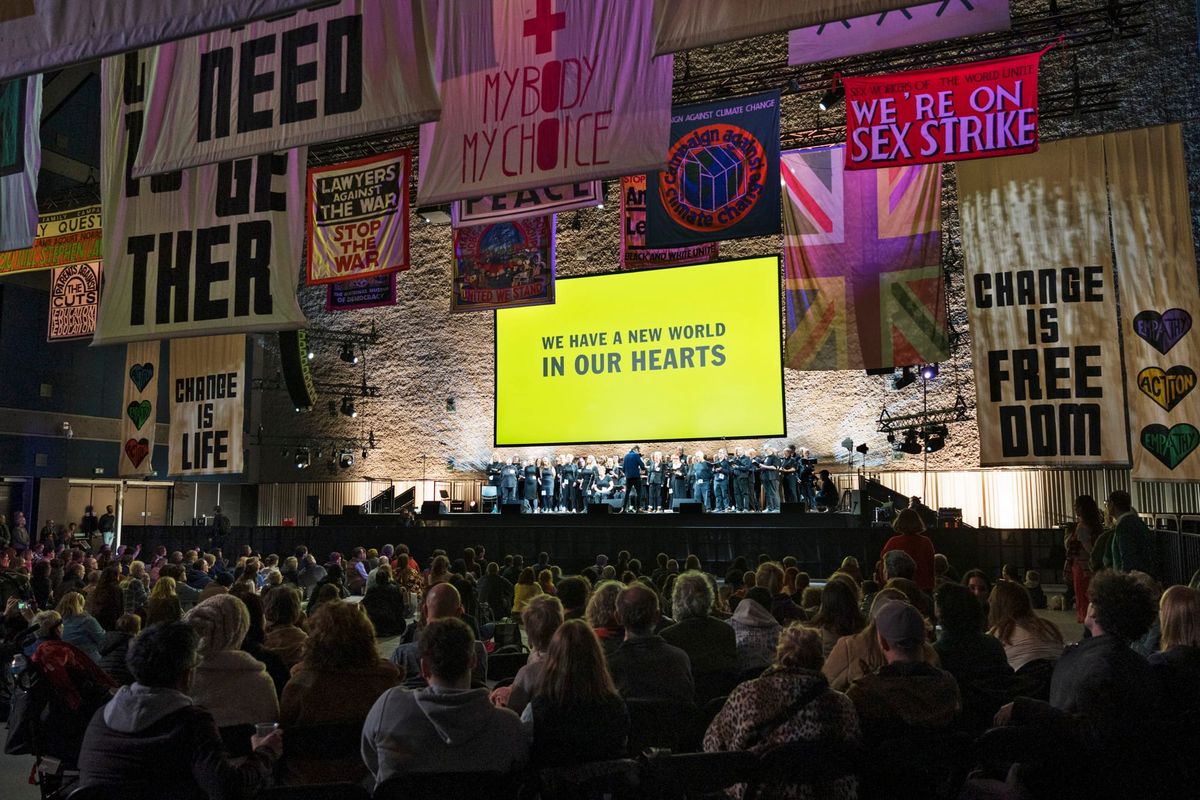 Commoners Choir performing at the Fête of Britain in Manchester with a projection reading “We have a new world in our hearts”