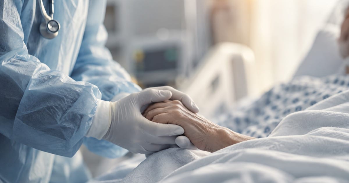 A clinician wearing protective equipment holds a hospitalized patient’s hand, illustrating physician risk and the duty to heal