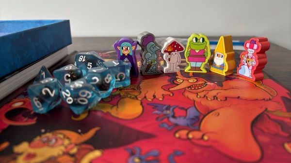 Blue transparent dice with a skull in them, cartoon meeples and a book with kinda dumb looking monsters from Land of Eem