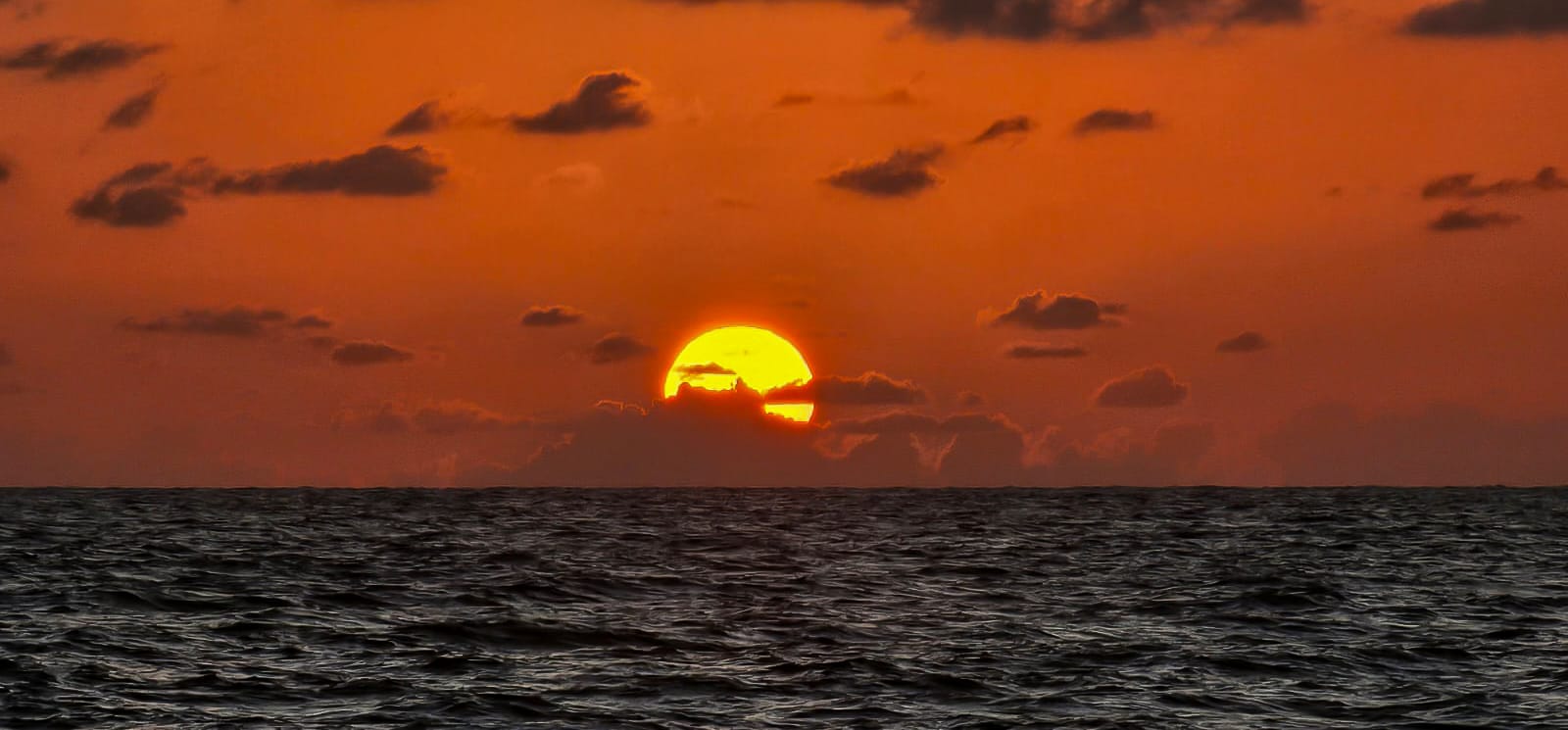 Golden hour over the sea — the sun slipping behind the clouds.