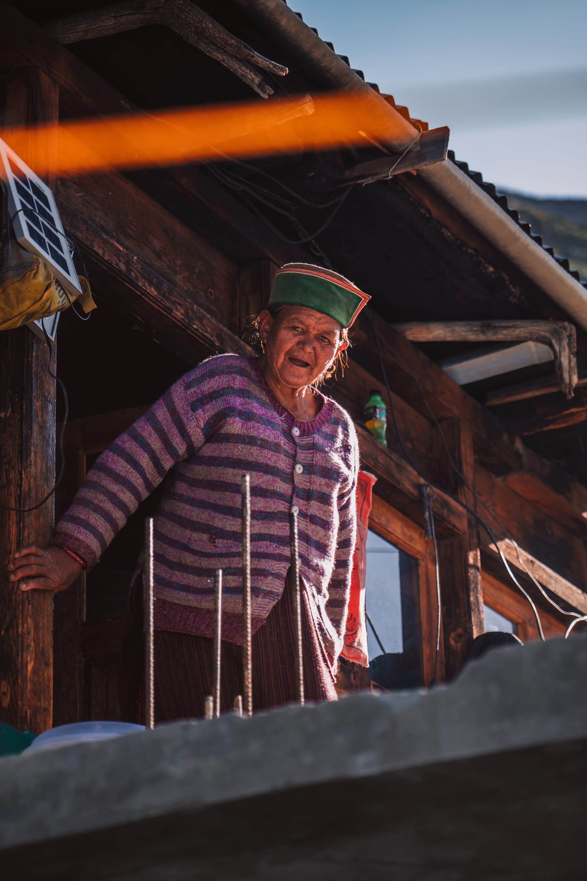 A smiling elderly man in a traditional Himachali cap in a village doorway