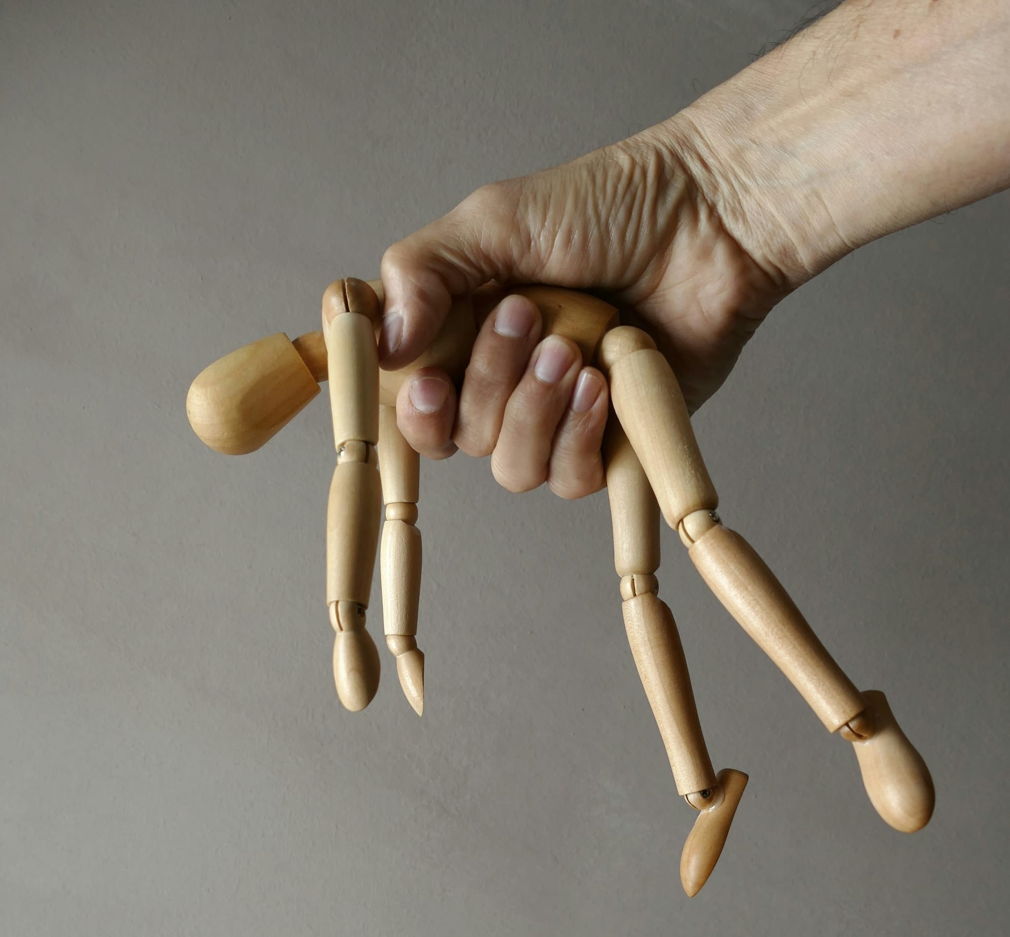A hand grasps a limp wooden manikin
