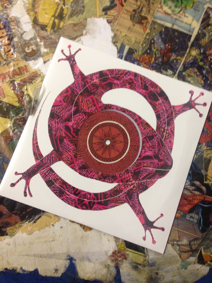 Cover of 'Feels Like' 10" - a coiled pink, orange & brown lizard with its head at the centre, its one visible eye with contrasting patterns forming the centre label of the 10" record