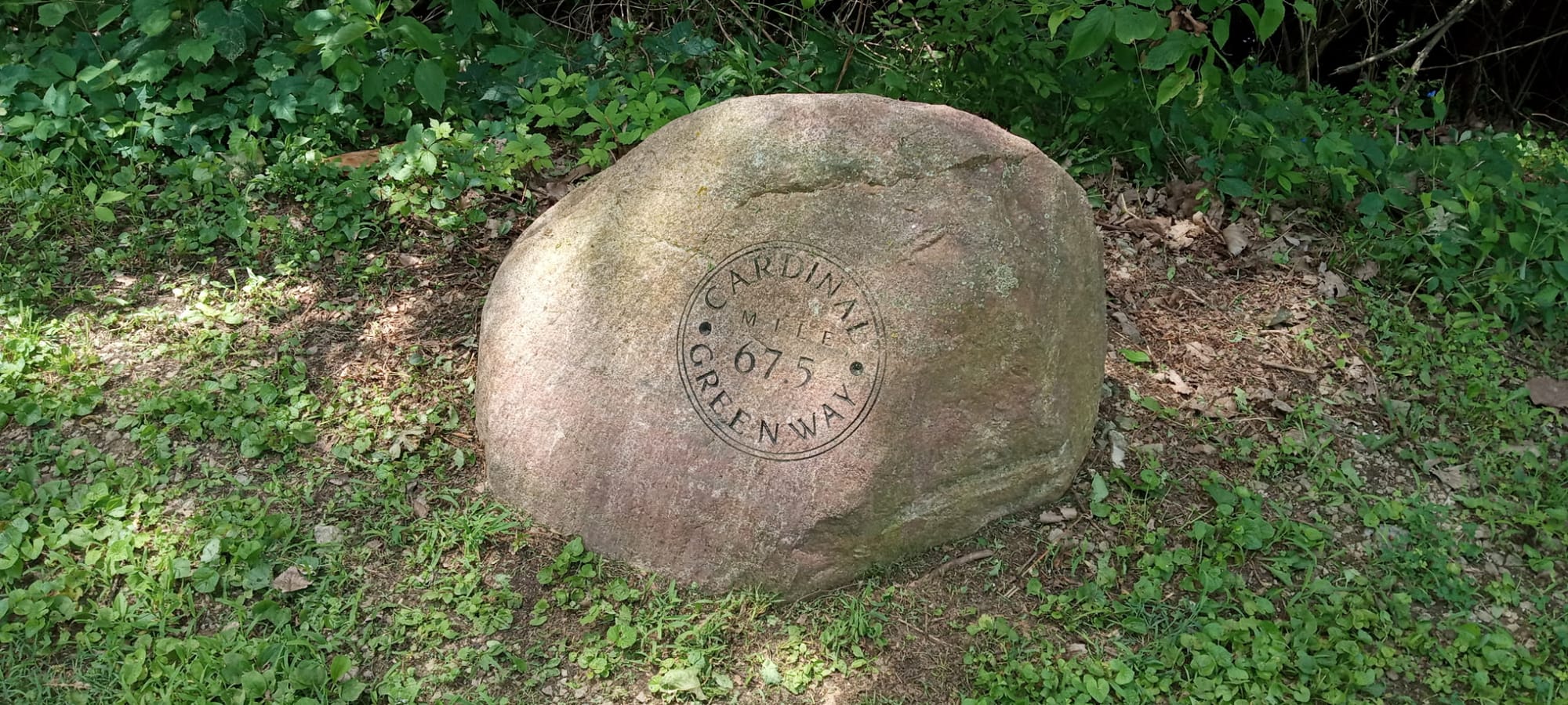 An engraved half-mile stone marker beside the paved Cardinal Greenway