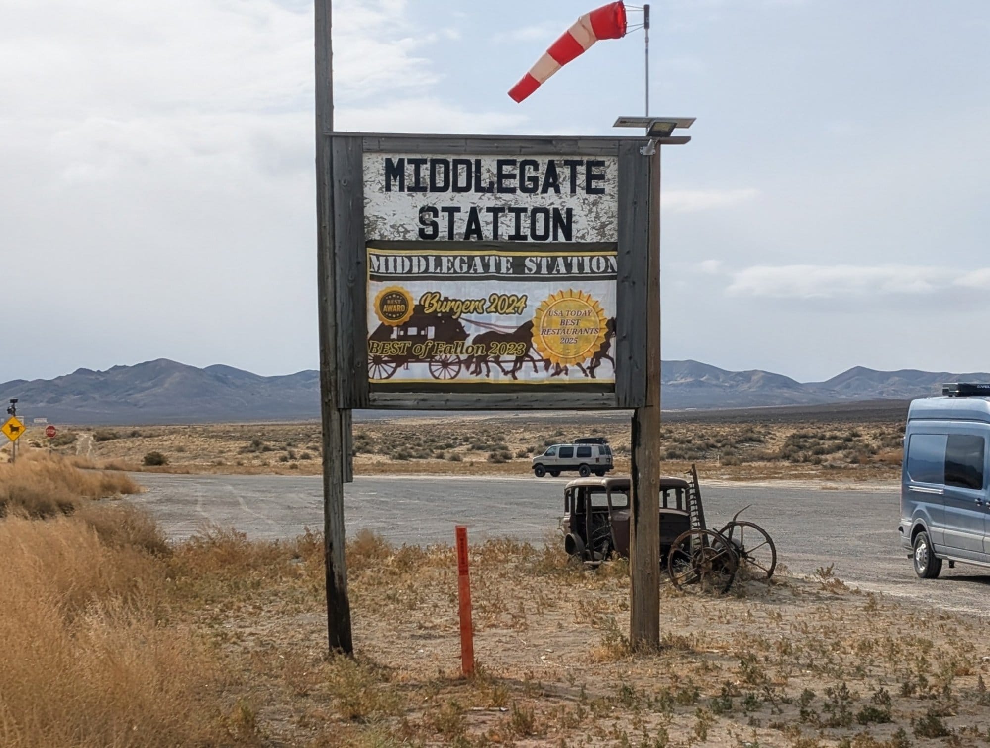The Middlegate Station roadside sign beside US 50, with an old wagon and desert hills behind it.