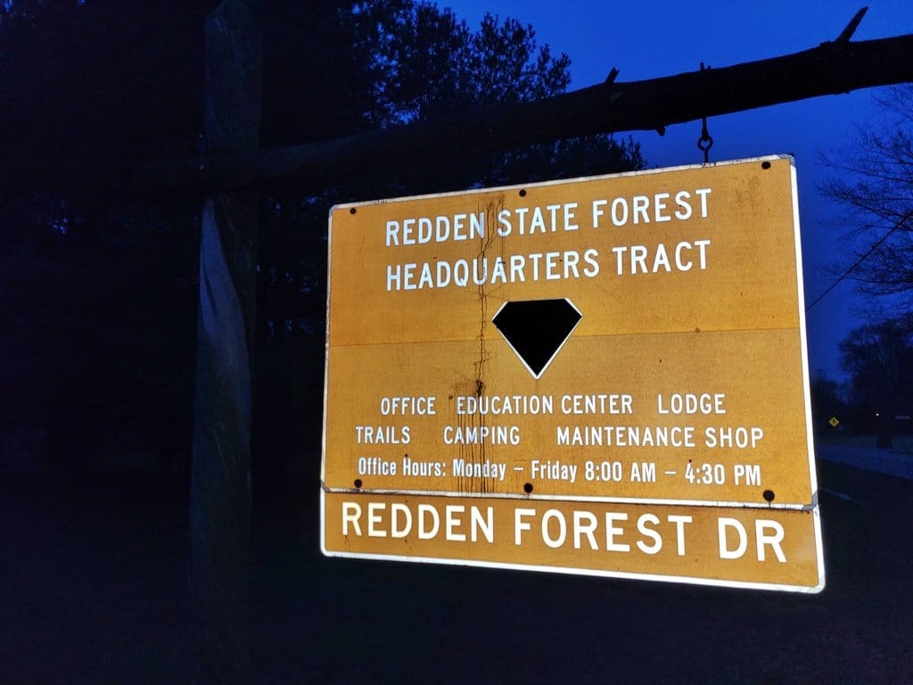 The Redden State Forest Headquarters Tract sign on Redden Forest Drive, lit against a dark blue evening sky.