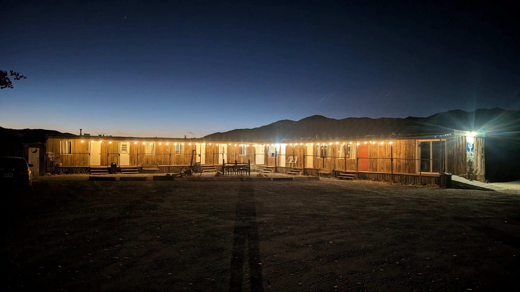 A long, low row of lit motel rooms under a deep blue dusk sky, with dark mountains behind.