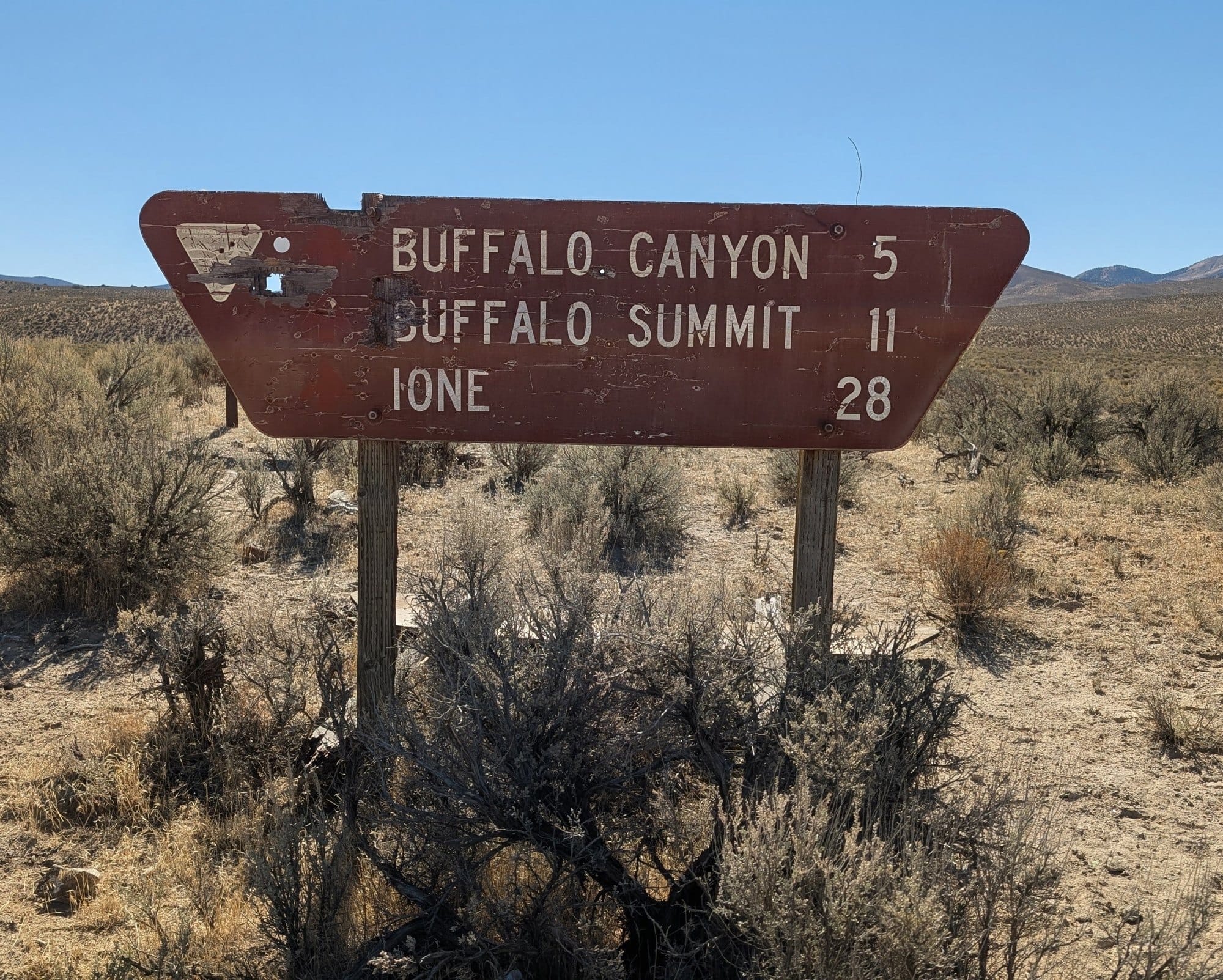 A worn wooden brown road sign in the sagebrush listing Buffalo Canyon 5, Buffalo Summit 11 and Ione 28.