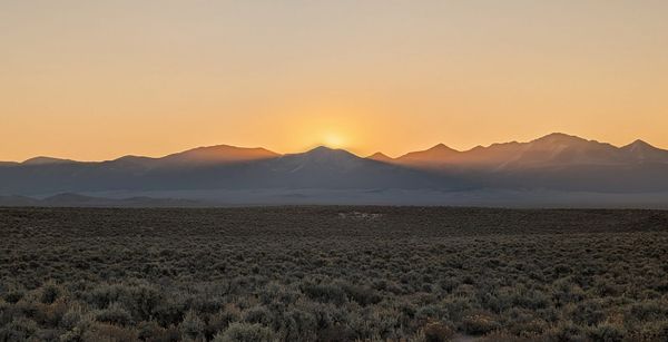 The sun rising over a jagged mountain range at the far edge of a wide, flat sagebrush valley