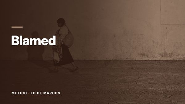 A woman carrying a bundle on her back walks past a yellow wall. Text: “Blamed”, Mexico: Lo de Marcos.