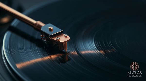 Close view of a copper record stylus on its arm, its tip on the groove of a dark navy record, a copper reflection on the grooves left of center, the right side dark.