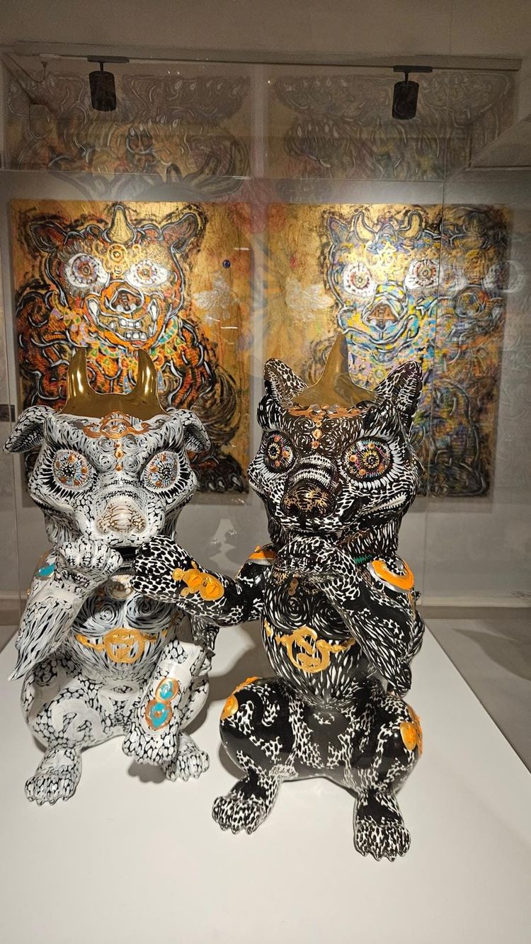 Two horned guardian sculptures, one white and one black, each covering its mouth with a paw