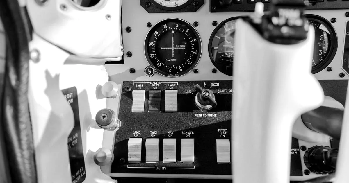 Aircraft cockpit control panel showing switches, gauges, and a yoke, viewed from the pilot's seat.