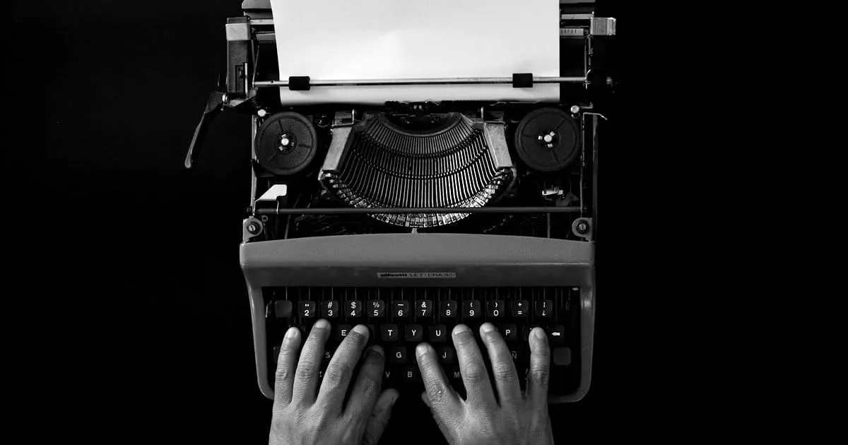 Two hands typing on a vintage typewriter loaded with paper, viewed from above on a black background.