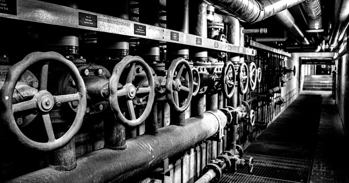 Rows of industrial valves and pipes in a corridor receding into the distance.