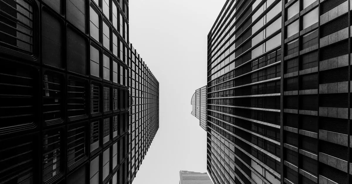 Looking up between two tall buildings with horizontal window grids stretching toward the sky, a third building visible at the bottom center.