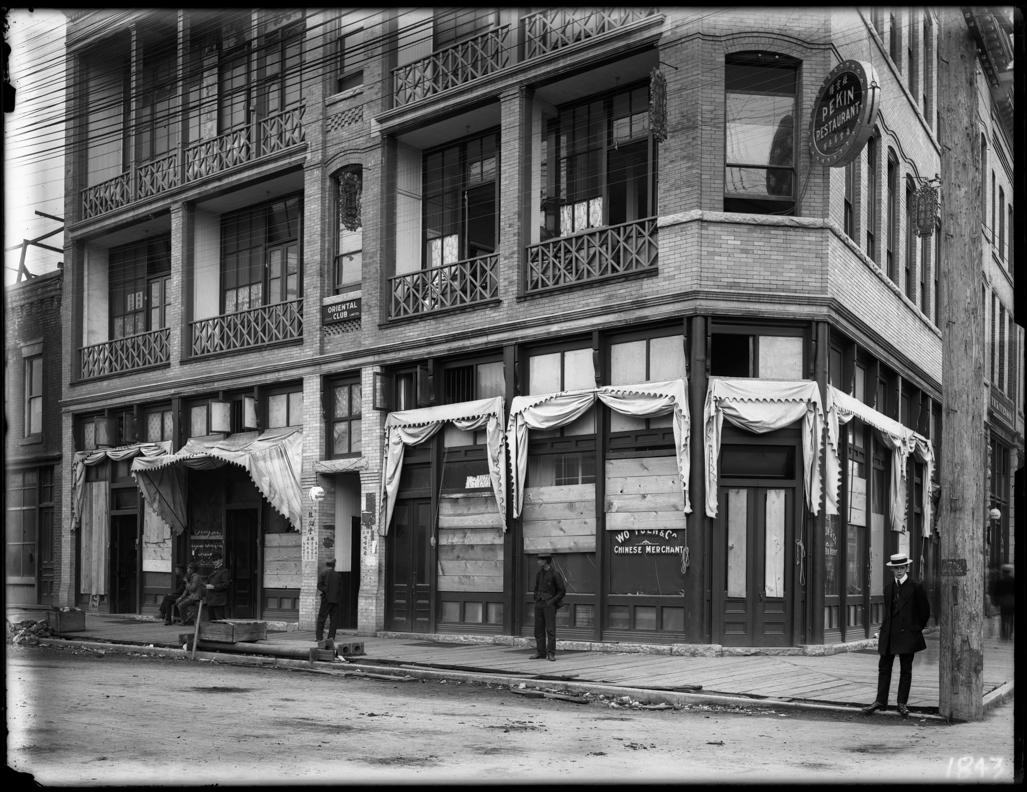 Boarded-up buildings in Chinatown, with a few scattered people standing around on the boardwalks in front of the building.