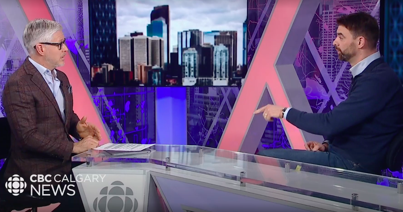 man in sweater over collared shirt points at man in suit