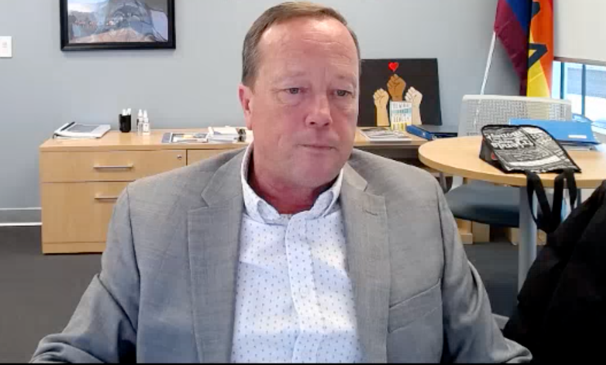 A middle-aged man in a grey suit jacket stares despondently at a downward angle, his mouth set closed.