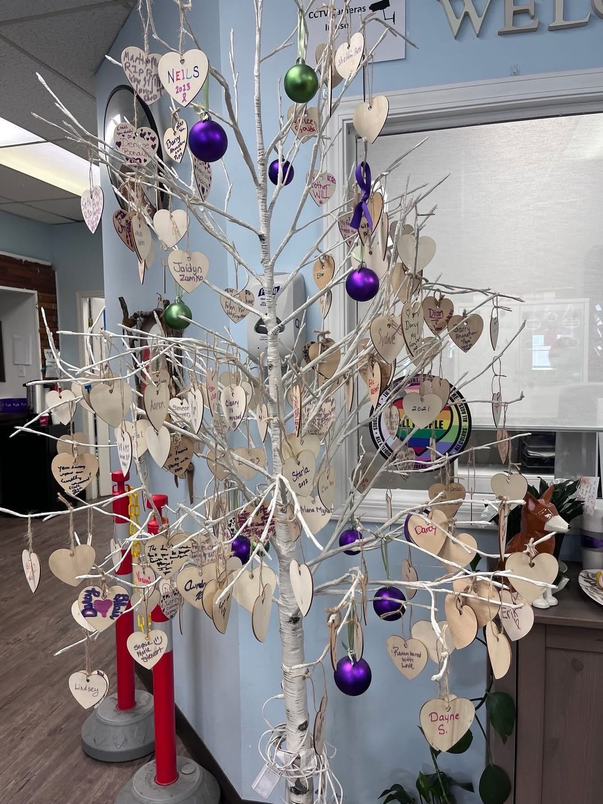 A small tree painted white with a hundred or more wooden hearts hanging from it, with people's names and short messages written on them.