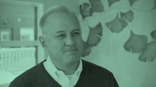 Green-tinted image of a man in a sweater over a white collared shirt.