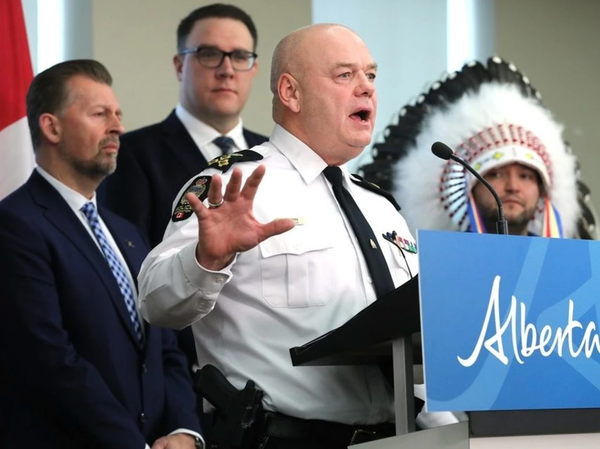 Police Chief Dale McFee speaks at a podium in a white shirt and tie with hand and mouth wide open.