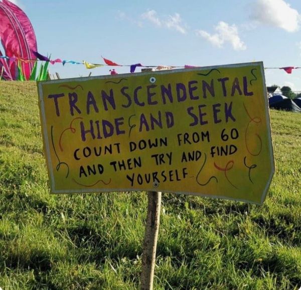 A hand-painted sign in a grassy field that reads "Transcendental hide and seek - count down from 60 and then try to find yourself"