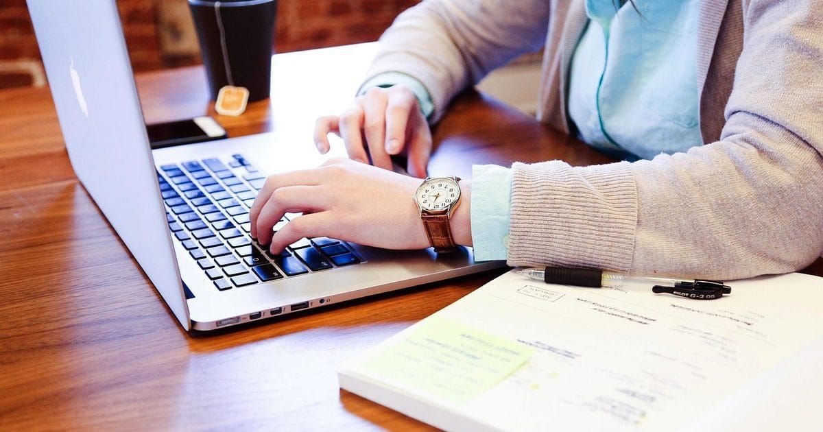 Person typing on a laptop at a wooden desk