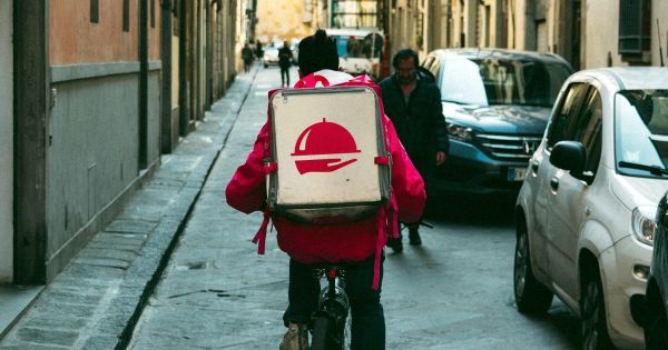 Bicycle courier with a red delivery bag riding down a city street