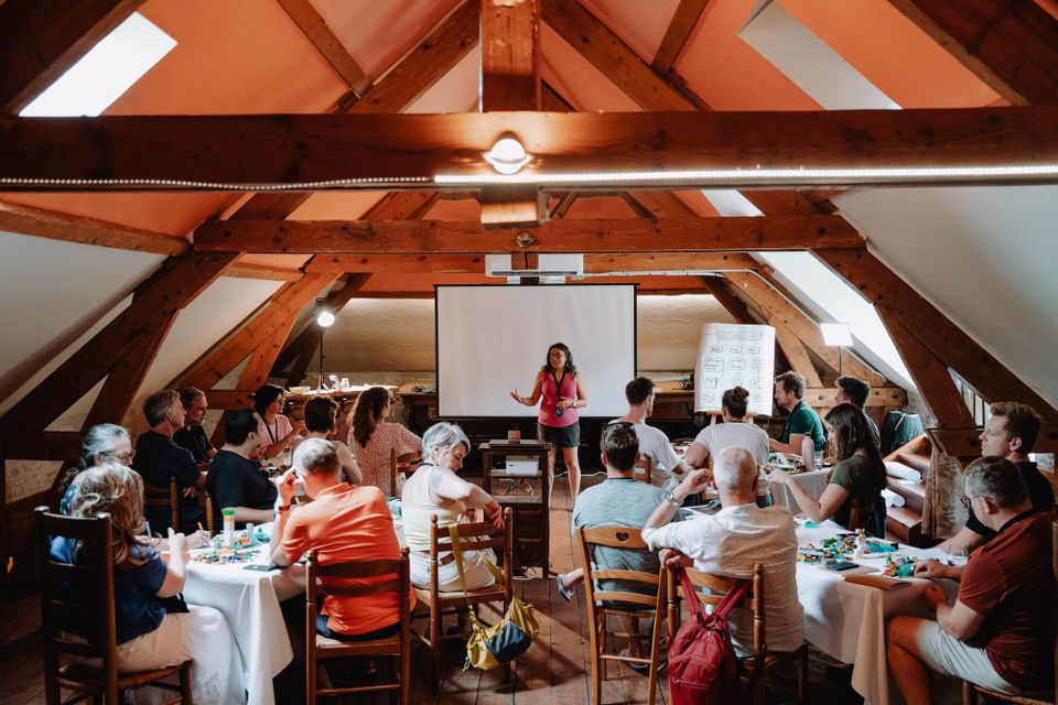 Angel standing up in a room full of people who are about to start a workshop with lego bricks 