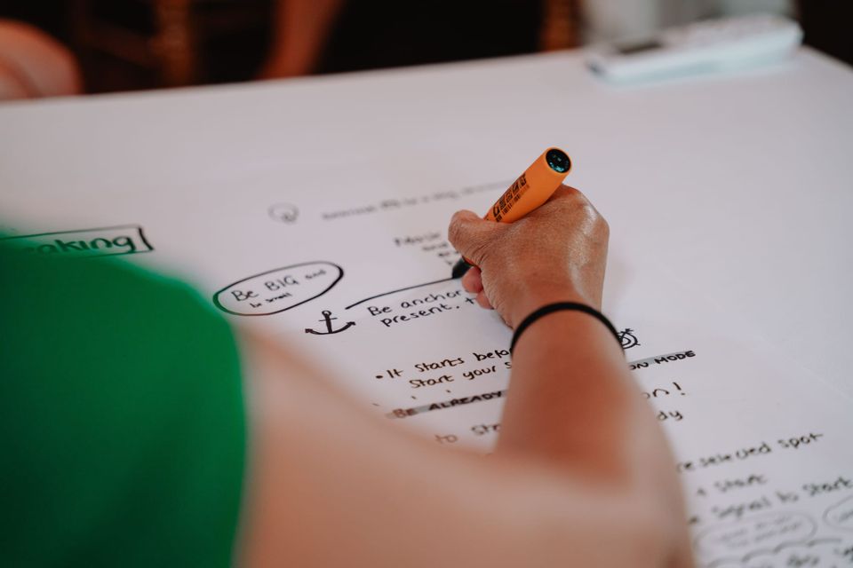 Angel is writing with a felt marker on a big sheet of paper to cover what is being spoken about