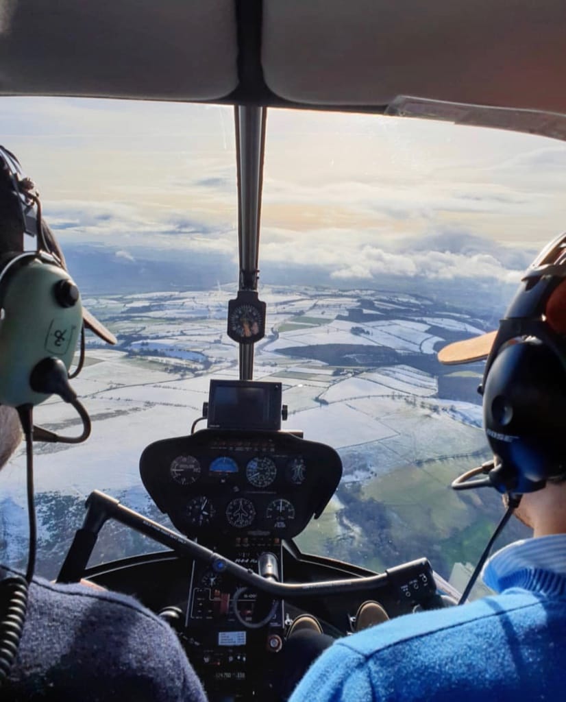 The instrument panel and view of snow-covered fields from the cockpit window of a Robinson R44 helicopter