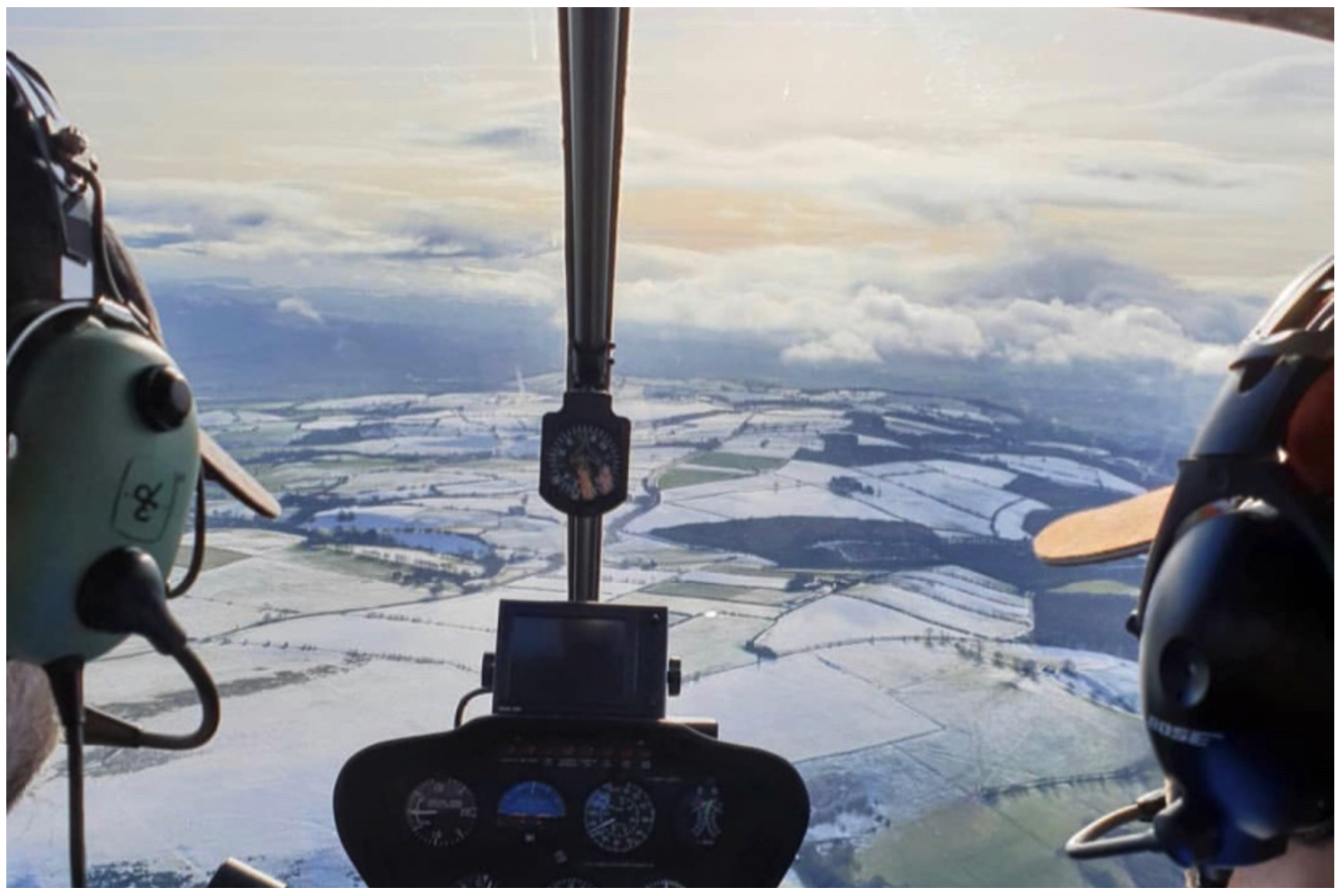 View forward out of the windshield of a Robinson R44 helicopter showing a pilot wearing a noise-cancelling (active noise reduction) headset and an and instructor wearing a passive headset  