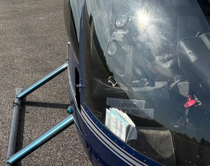 The windshield of Robinson R44 helicopter viewed from outside. A tablet suction mount is visible on the inside of the windshield. 