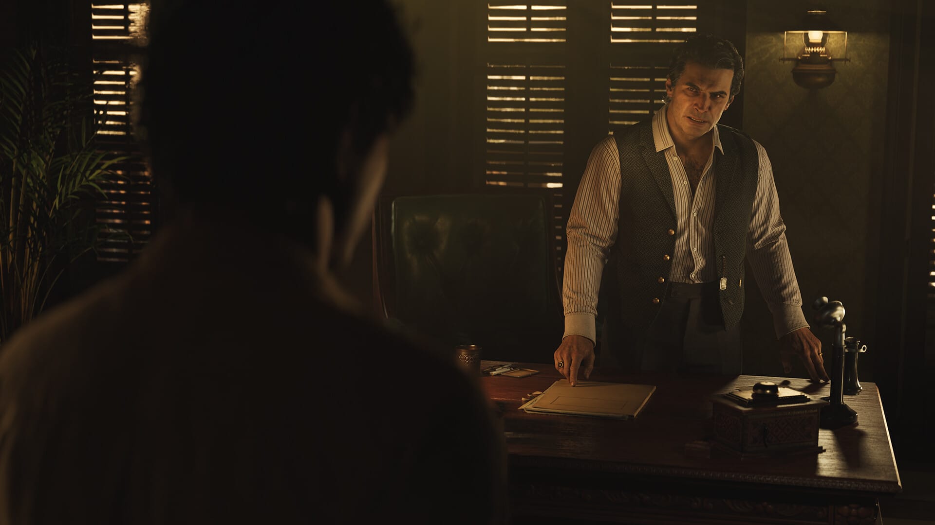 Don Torrisi, a man dressed in a vest, stands over a desk. A sconce in the background illuminates a dark room.
