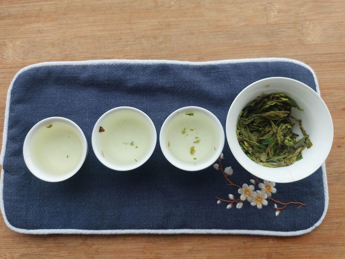 A gaiwan with tea leaves with three small cups of tea
