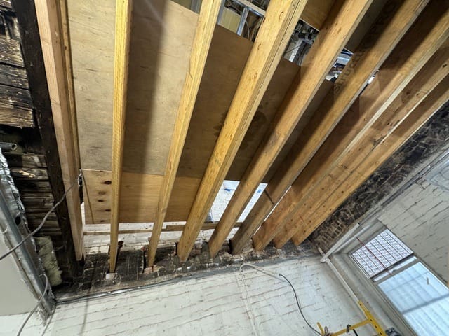New 1¾-inch by 9½-inch engineered LVL joists, bolted in pairs and seated in the original masonry pockets. Once the subfloor and the ceiling below are restored, none of this structural work will be visible.