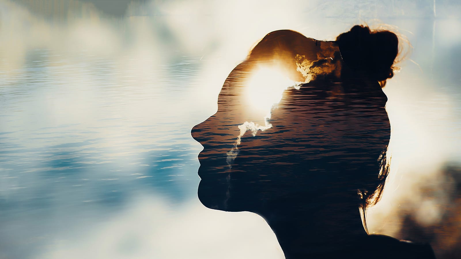 Silhouette of a person's head filtering sunlight breaking through clouds with rippling water in background..