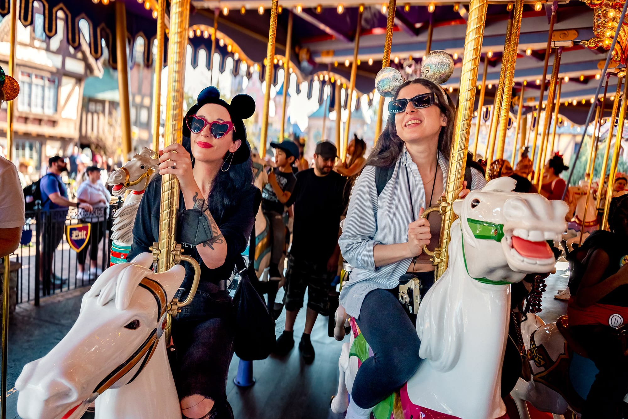 Two ladies in sunglasses and mouse ears astride their carousel steeds in Disneyland, California