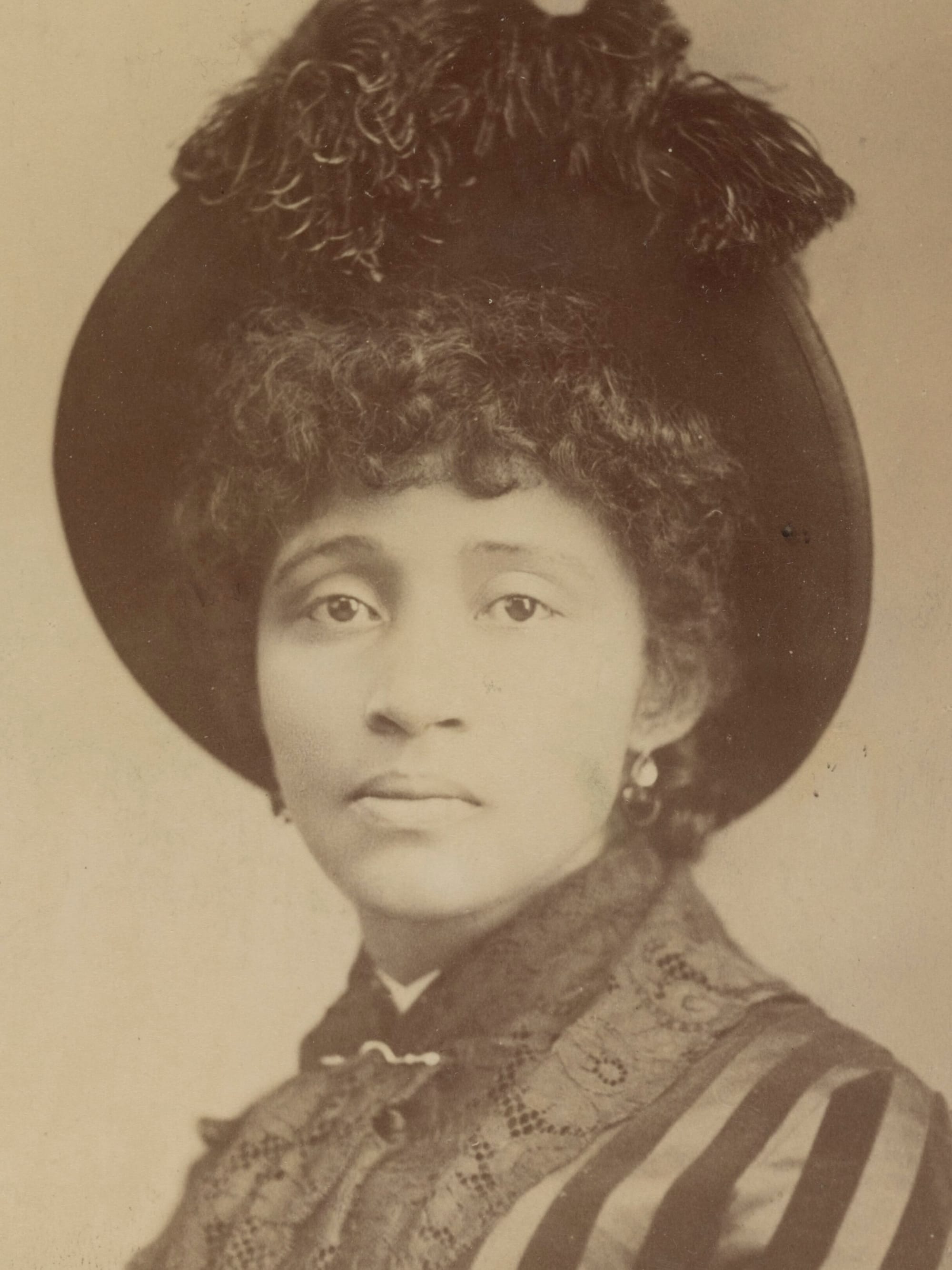 An 1886 photograph of Lucy Parsons (1851-1942) in a large, handsome feathered hat, with dark curly hair and a sad, beautiful expression